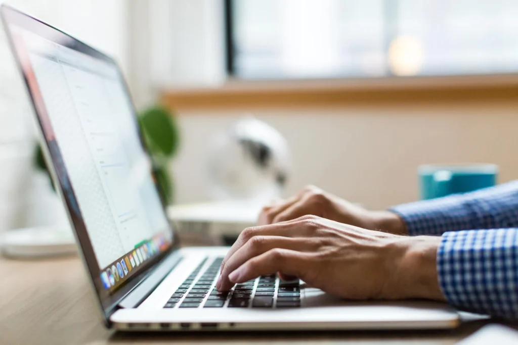 Homem com camisa xadrez digitando no notebook procurando informações sobre lançamento