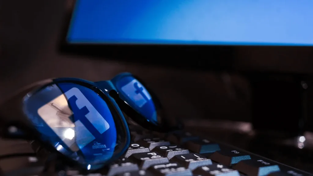 Óculos sobre uma tecla de computador refletindo o logo do Facebook nas duas lentes