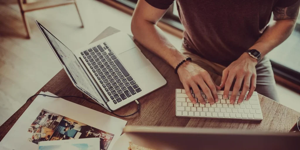 Homem digitando no computador com notebook ao lado