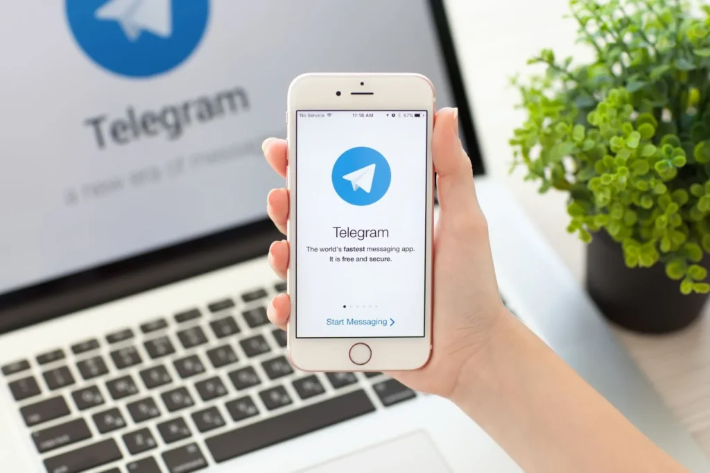 Pessoa segurando celular aberto no Telegram e notebook aberto na versão desktop da plataforma